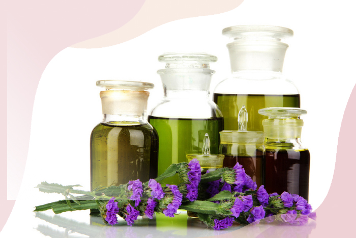 Various sized bottles of essential oils and green herbal extracts, accompanied by vibrant purple flowers, illustrating the natural remedies available at HEAAL Homeopathy Clinic in Hyderabad.